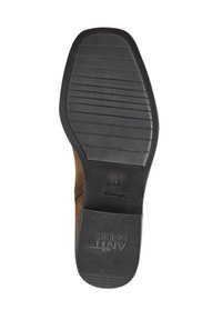 Botte en suede marron avec une semelle en caoutchouc noir texturé dotée de rainures horizontales et de marquage, conçue pour offrir adhérence et durabilité.
