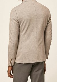 Beiger Blazer mit Muster und tailliertem Schnitt, ausgestattet mit einem Reverskragen, zwei Knöpfen am Ärmel und einer glatten Textur.