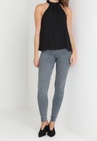 Svart halterneck-topp med en flödande design, kombinerad med åtsittande grå skinny jeans. Modellen bär svarta klackskor. Enkelt och stilrent outfit.