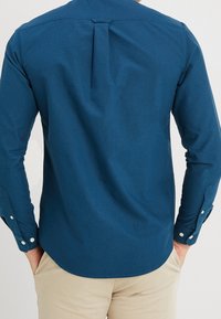 Męska koszula z długim rękawem w głębokim niebieskim kolorze, uszyta z gładkiego materiału. Posiada karczek z tyłu, dopasowany krój oraz mankiety na guziki.