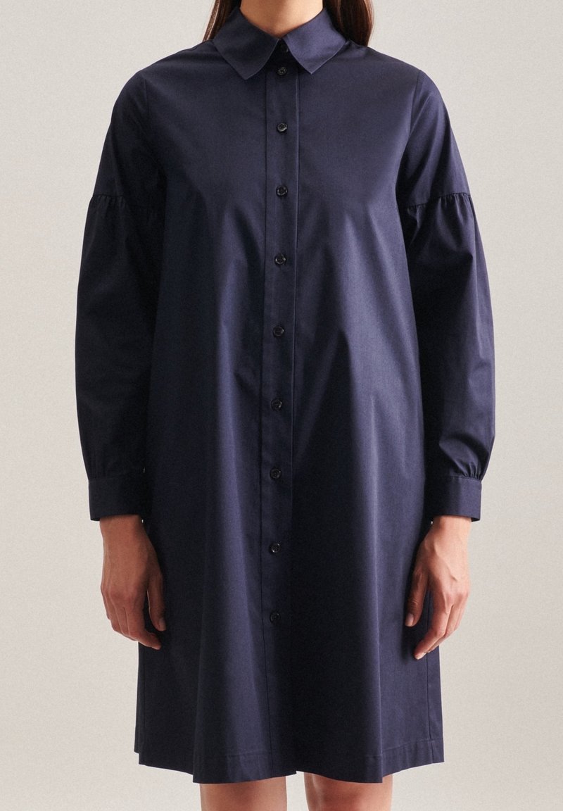 Námořnická modrá košilová šaty s límečkem, dlouhými rukávy a nabranými detaily na ramenou, vyrobené z hladké tkaniny.
