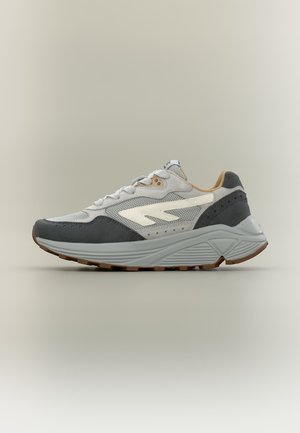 Zapatilla deportiva de corte bajo con malla gris y negra, detalles de cuero blanco, interior beige y suela gruesa texturizada gris.