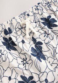 Floral bestickte Shorts in Creme und Marineblau. Elastischer Bund mit verstellbarem Kordelzug. Verziert mit aufwendigen Blumenmustern und Textur.