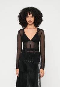 Fekete áttetsző, hosszú ujjú felső, mély dekoltázzsal és estruturált fazonnal, fényes részletekkel és rétegezett kialakítással. Fekete műbőr szoknya, textúrával.