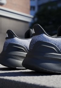 Des sneakers avec une tige texturée grise et noire, dotée d'un col rembourré et d'une semelle noire robuste avec un motif de motif sur la semelle.
