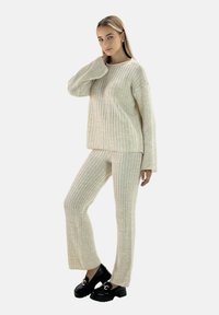 Beżowy sweter w prążki i dopasowane spodnie, dzianinowa tekstura, luźny krój, długie rękawy, noszony z czarnymi butami na platformie z ozdobnym wykończeniem.