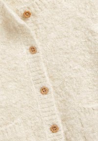 Tissu tricoté doux de couleur crème avec un motif texturé comportant quatre boutons en bois marron clair alignés verticalement.