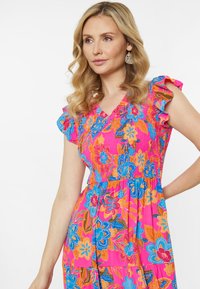 Levendig roze jurk met bloemenpatronen in blauw, oranje en groen. Kenmerkt zich door gerimpelde mouwen en een gerimpelde boezem, van lichtgewicht stof.