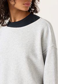 Hall hallipluus, millel on must ümmargune kaelus ja langevate õlgadega disain. Pehme tekstuur ja vabaaja stiilis väljund, õmmeldud detailid varrukatel.