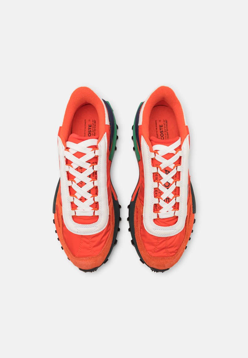 Un par de zapatillas deportivas en naranja, blanco y verde con cordones blancos, suelas texturizadas y logotipos impresos en la zona del talón.