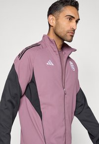 Μωβ και μαύρο αθλητικό ζακέτο με φερμουάρ, που διαθέτει ψηλό γιακά, κεντημένο λογότυπο και πλαϊνές τσέπες, κατασκευασμένο από ελαφρύ, υφασμάτινο με υφή.