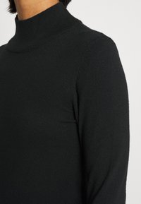 Svart polotröja med en åtsittande design, slät textur och ribbade detaljer vid kragen, som visar en ren, minimalistisk look.