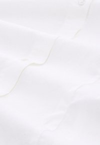 Witte stof met een gladde textuur, met subtiele stiksels en een knoopdetail, tentoongesteld in zachte plooien.