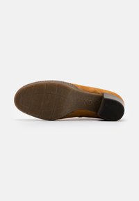Suela de zapato de ante marrón con un agarre de goma texturizada, con un pequeño tacón y un detalle de costura visible a lo largo del borde.