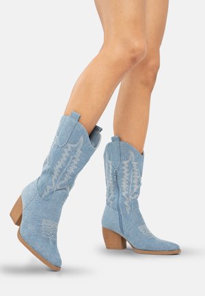 Botas de vaquero de denim azul con detalles de costura blanca, punta redondeada y tacón cuadrado, con cremallera lateral y lengüetas de agarre.