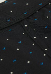 Černá látka s opakujícím se vzorem malých, barevných geometrických tvarů v modré a bílé. Textura je hladká a mírně pružná.