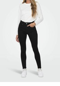 Černé skinny džíny s vysokým pasem, designem na pět kapes a zapínáním na knoflík. V kombinaci s bílou košilí s dlouhými rukávy a bílými teniskami.