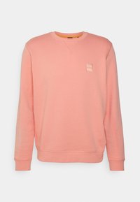 Růžová mikina z měkkého materiálu; má dlouhé rukávy, kulatý výstřih a malé vyražené logo na hrudi. Oranžový vnitřní lem.