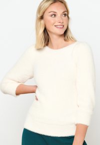 Puhast bela pulover s okroglo zasnovo in rokavi do 3/4, ki ima mehak teksturo in prilegajoč rob. Uporabljen z turkiznimi hlačami.