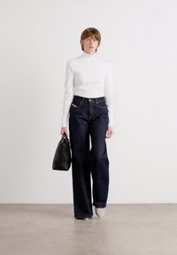 High-waisted dark denim jeans paired with a fitted white turtleneck, holding a black quilted handbag. Simple background texture.
