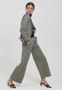 Costume à carreaux vichy en noir et blanc avec un blazer ajusté et un pantalon à jambe large, associé à des talons ouverts noirs. Texture de tissu lisse.