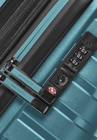 Maleta rígida en tono azul verdoso con detalles en negro. Cuenta con dobles cremalleras con empuñaduras azules, candado aprobado por la TSA y superficie texturizada para mayor durabilidad.