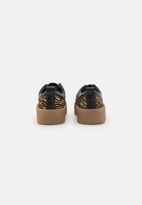 Sorte lær sneakers med zebra mønster på sidene, beige gummisåler og svarte hæltabber. Glatt tekstur gjennom hele.