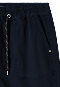 Pantalones cortos azul marino con cintura elástica, cordón blanco y negro, y gran bolsillo delantero con detalle de remache metálico.