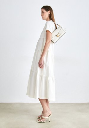 Bela bomba iz bombaža z več plastmi, kratkimi rokavi in tekočo silhueto. V kombinaciji s strukturirano kremo torbico in svetlimi salonarji.