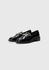 Zwarte lakleren loafers met een lage blokhak, met een decoratieve zilveren gesp aan de voorkant en een gladde, glanzende afwerking.