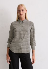 Chemise boutonnée tissée à motif géométrique noir et blanc, dotée d'un col et de manches longues, associée à un pantalon noir.