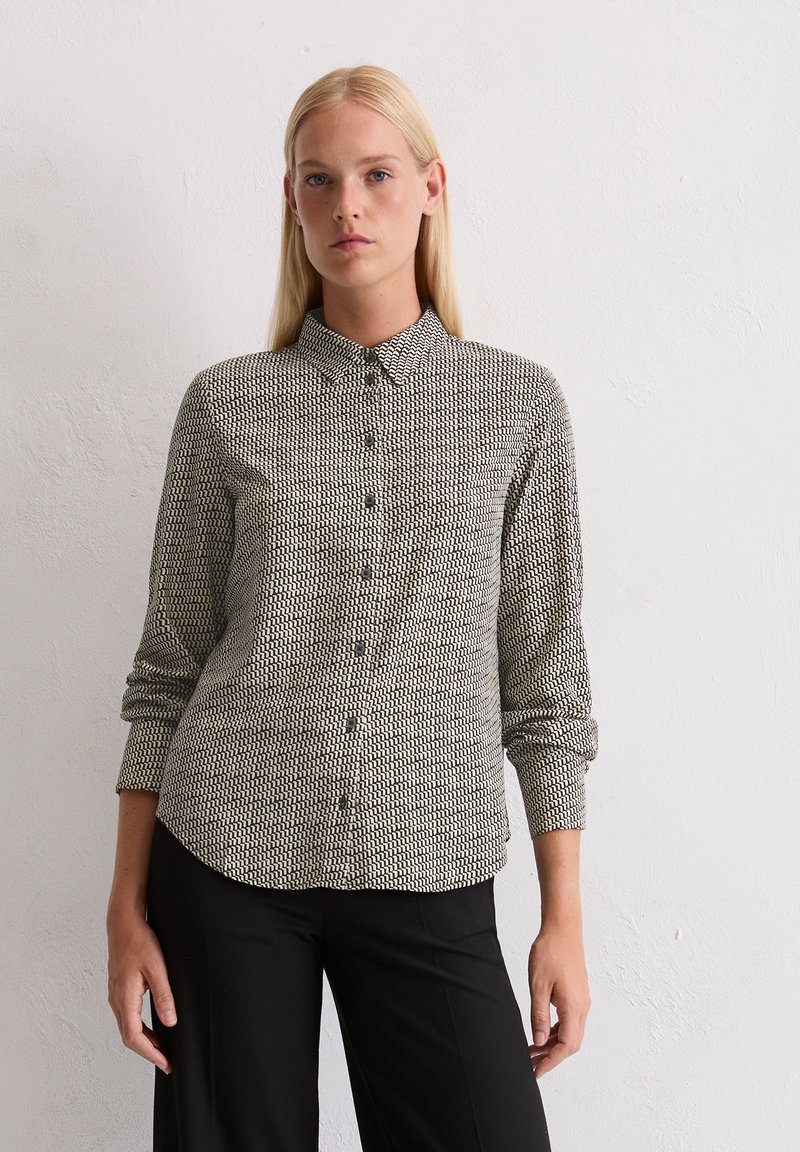 Chemise boutonnée tissée à motif géométrique noir et blanc, dotée d'un col et de manches longues, associée à un pantalon noir.