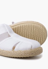 White canvas espadrille with an open toe design, featuring a woven jute sole and textured rubber outsole. Visible stitching and cut-outs.
