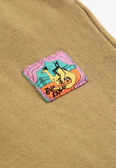 Patch en tissu carré avec une girafe dessin animé portant un chapeau et des bottes noires sur fond orange, sarcelle et rose cousu sur un textile marron.