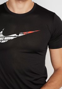 Musta urheilu t-paita, jossa on lyhythihainen malli ja suuri valkoinen ja punainen Nike-swoosh-logo rinnan alueella, sileä kangas.