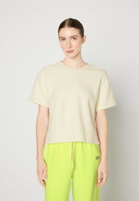 T-shirt corto color crema con tessuto texturizzato, scollo rotondo e vestibilità morbida, abbinato a pantaloni verde brillante con cordino.