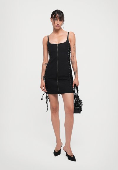 Black sleeveless dress with a front zipper and lace-up details on the sides. The fabric is smooth, and the design is fitted to the body.
