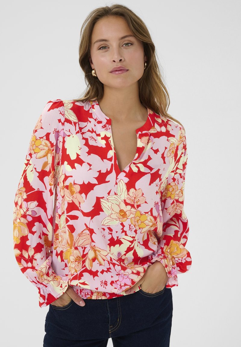 Virágmintás, hosszú ujjú blúz piros és rózsaszín mintával, V-kivágással és ráncolt mandzsettákkal, könnyű anyagból készült.
