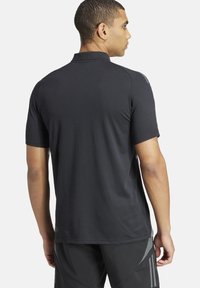 Zwarte polo met korte mouwen van een gladde stof, met een klassieke kraag en subtiele schouderaccenten.