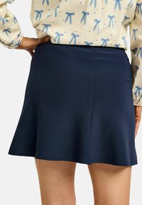 Mornarsko modra razširjena krilo iz gladkega blaga z enostavno zasnovo in subtilnimi detajli roba. Pogled od zadaj prikazuje elegantno obliko.