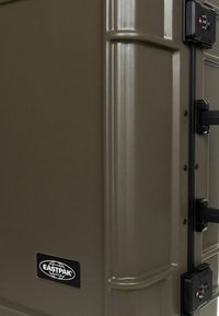 Eastpak hard-shell suitcase in matte olive green, featuring a textured finish, black locking mechanism, and prominent brand logo.