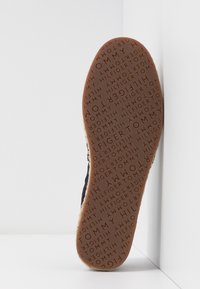Semelle d'une chaussure marron avec un motif de texte "TOMMY HILFIGER" répété dans différentes orientations sur fond blanc.