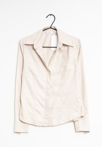 Camicia beige a maniche lunghe con colletto, caratterizzata da una texture liscia, vestibilità sartoriale e motivo rigato verticale. Appesa a un gancio nero.