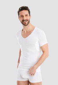 White short-sleeve v-neck t-shirt with a soft texture, featuring a fitted design and slight side cut-outs. Worn with white boxer shorts.