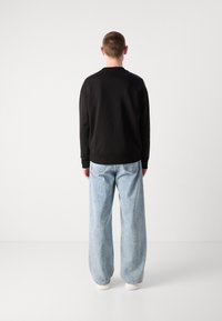 Sudadera negra con puños y dobladillo acanalados, combinada con jeans de pierna ancha de color azul claro. Textura de tela suave, diseño casual.