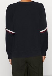 Felpa nera con maniche raglan e accenti a righe contrastanti in rosso e bianco ai polsini. Tessuto morbido e strutturato.