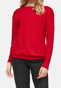 Red, long-sleeve sweater with a textured pattern and ribbed hem. Loose fit and crew neckline. Worn with black pants.
