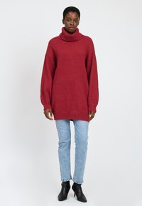 Rød oversized turtleneck sweater i blødt, struktureret strik, parret med lyseblå jeans og sorte hælede støvler. Simpelt design, afslappet pasform.