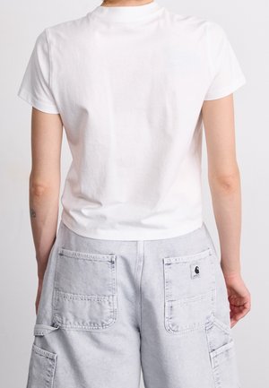 Persona vistiendo una camiseta blanca sencilla de manga corta y pantalones cortos tipo cargo de color gris claro con bolsillos traseros, mostrada desde atrás sobre un fondo blanco.