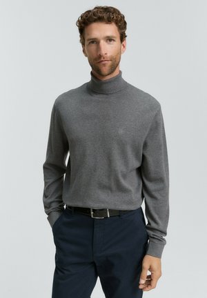 Jersey de cuello alto gris hecho de una tela suave, con mangas largas y una silueta ajustada, combinado con pantalones azul marino oscuros y un cinturón negro.